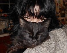 a woman with black hair holding a cat in her arms