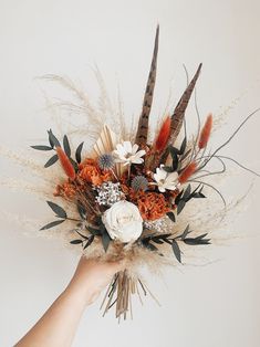 a hand holding a bouquet with feathers and flowers in it's centerpiece, against a white background