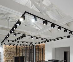 an empty room with lots of windows and lighting fixtures on the ceiling, in front of a brick wall