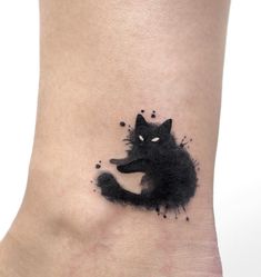 a black cat tattoo on the ankle with ink splatters all over it's body