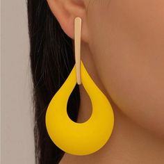 a close up of a person wearing large yellow earrings with wooden sticks in the shape of a tear