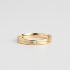 a yellow gold wedding band with a single diamond in the center, on a white background