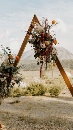 an arch decorated with flowers and greenery stands in the middle of a desert landscape