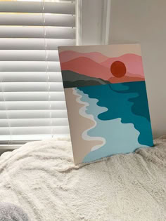 an acrylic painting sitting on top of a bed next to a window