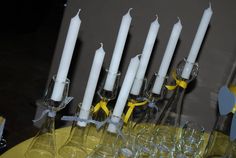 a table topped with lots of wine glasses next to tall white candles and yellow napkins