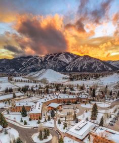 an aerial view of a town surrounded by snow covered mountains and trees at sunset or dawn