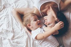 a mother and her son laying on the bed looking at each other while they cuddle