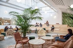 people are sitting in chairs and sofas in an open space with plants on the floor