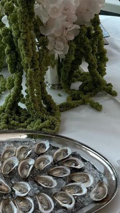 a platter filled with oysters on top of a table next to white flowers