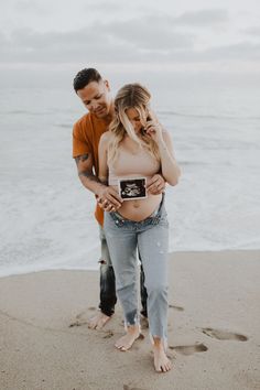 a pregnant woman standing next to a man on the beach