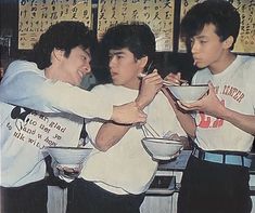 three young men standing together holding bowls and chopsticks