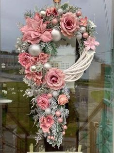 a wreath with pink flowers and silver ornaments hanging in front of a storefront window