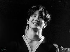 a black and white photo of a woman with short hair wearing a necklace smiling at the camera