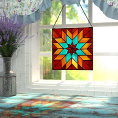 a colorful stained glass sun catcher hanging from a window sill next to a vase with purple flowers