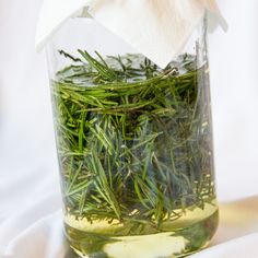 a glass jar filled with green herbs on top of a white cloth covered tablecloth