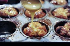 a person pouring sauce on some cupcakes in a muffin tin filled with them