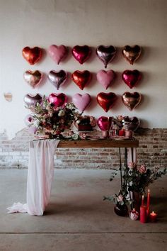 a table topped with lots of pink and red heart balloons next to a brick wall