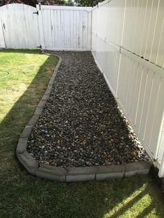 a white fence next to a yard with rocks and grass on the ground in front of it