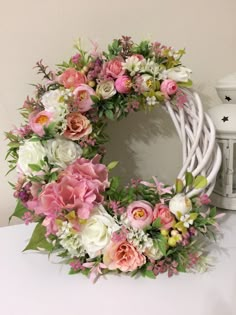 a white wicker wreath with pink flowers and greenery on the front, sitting on a table