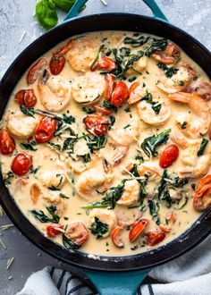 a skillet filled with shrimp, tomatoes and spinach on top of a table