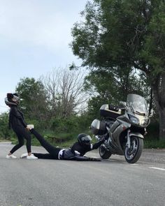 a person laying on the ground next to a motorcycle and another person standing over it