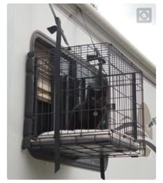 a black cat sitting in a cage on the side of a building