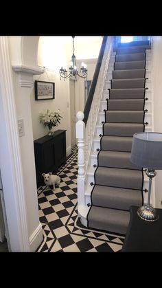 a staircase with black and white checkered flooring, chandelier and lamp