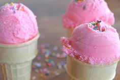 three ice cream cones with sprinkles and pink frosting, on a table