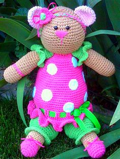 a crocheted teddy bear wearing a pink dress with polka dots on it sitting in the grass