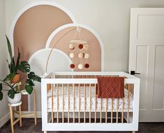 a baby crib in a pink and white nursery with an arch wall hanging from the ceiling