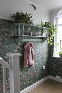 a coat hanging on a wall next to a window with plants in it and a planter