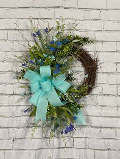 a wreath with blue flowers and greenery hangs on a brick wall