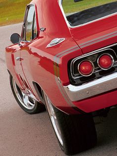 a red car parked on the side of a road next to a grass covered field