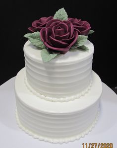 a three tiered white cake with a purple rose on the top and green leaves