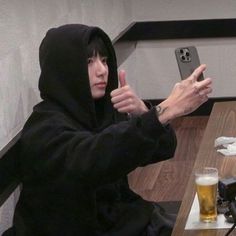 a man in a hoodie sitting at a table with a cell phone and beer