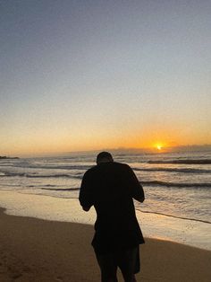 a man standing on top of a sandy beach next to the ocean at sun set