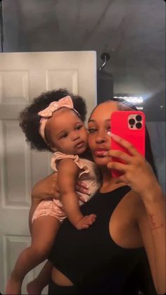 a woman holding a baby taking a selfie in front of a mirror with her cell phone