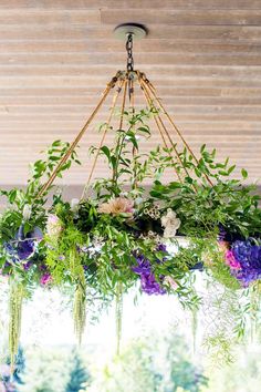 a chandelier filled with flowers and greenery hanging from it's ceiling