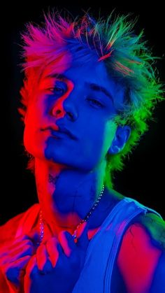 a man with colorful hair and piercings standing in front of a black background wearing a white tank top