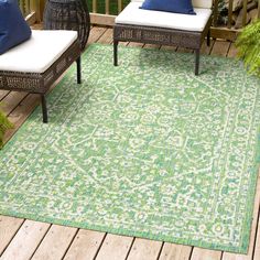 a green rug on a wooden deck with two white chairs and blue pillows in the background