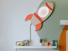 an orange and white rocket ship shaped lamp on a wall above a shelf in a children's room