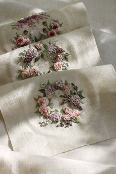 three embroidered napkins with flowers on them sitting on a white cloth covered tablecloth