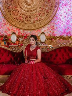 a woman in a red gown sitting on a couch with flowers behind her and the backdrop is