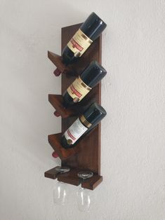 three wine glasses are placed on a wooden shelf holding several bottles and two empty wine glasses