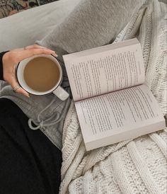 a woman sitting on a couch holding a cup of coffee and an open book in her lap