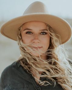 a woman with long blonde hair wearing a hat and looking at the camera, outdoors