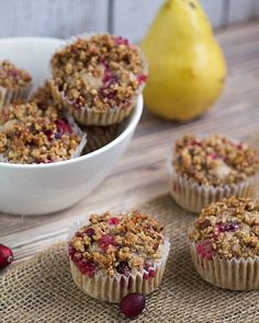 several muffins with cranberry topping sit on a table next to a pear