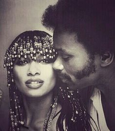 a black and white photo of a man kissing a woman's forehead with beads on her head