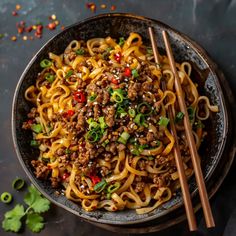 a bowl full of noodles with chopsticks on the side and green onions in the middle