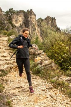 a woman running down a rocky trail in the mountains with her back pack and backpack on